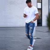 Young man wearing Deep Blue Hole Men’s Jeans with high-quality cotton, ripped style, and colorful sneakers