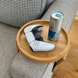 White DualSense controller on bamboo clip-on sofa armrest tray with Fiji water