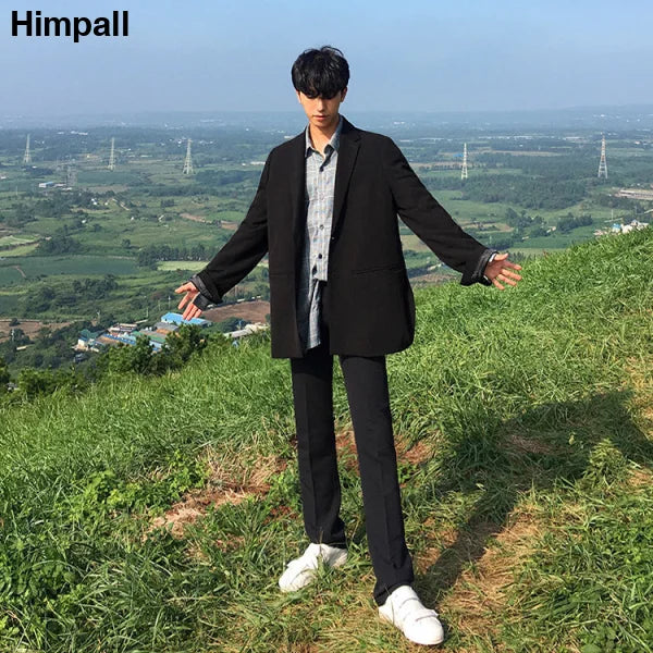 Young man in black suit and white sneakers showcasing solid color casual pants on hillside