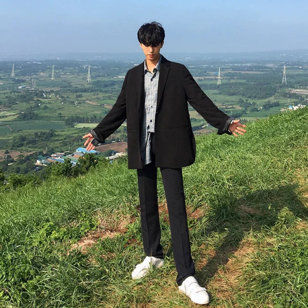 Young man in black suit and white sneakers showcasing solid color casual pants on hillside
