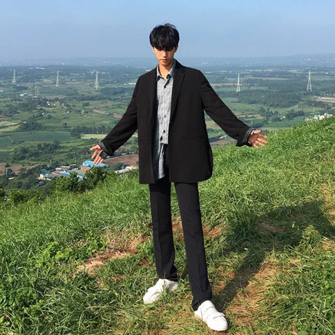 Young man in black suit and white sneakers showcasing solid color casual pants on hillside