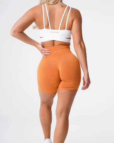 Orange high-waisted Nvgtn Seamless Pro Spandex Shorts with white sports bra
